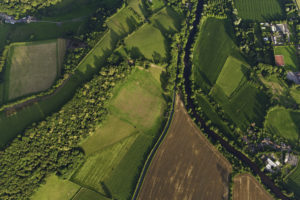 Tętniące życiem zielone uprawy, zaorane pola i pastwiska, żywopłoty i lasy otaczające farmy i wiejskie domy obok idyllicznego wiejskiego krajobrazu z góry.